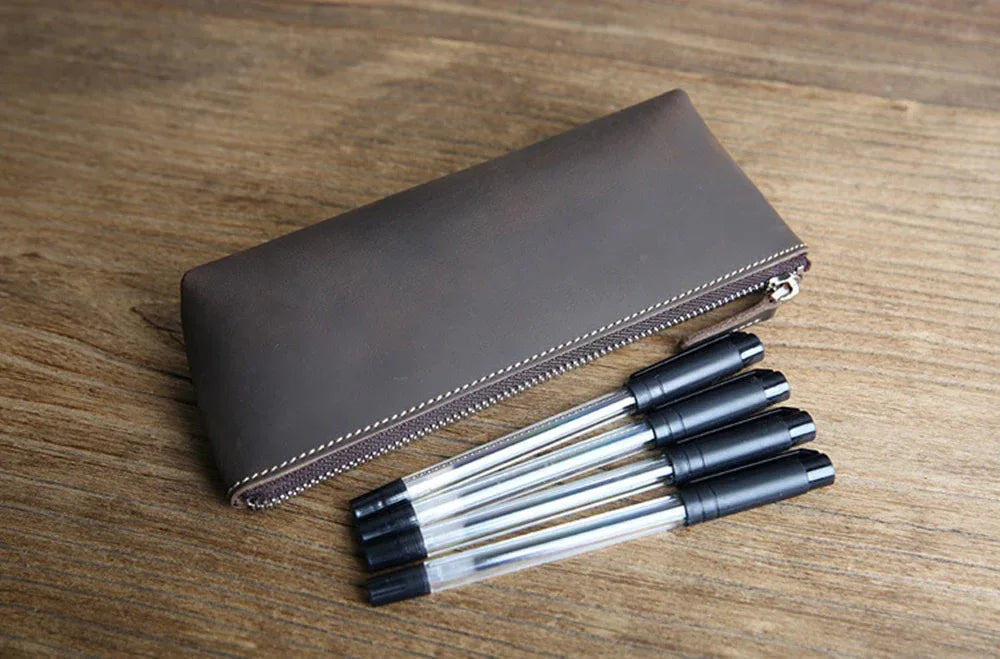 Brown leather pencil case on table with zipper, next to black pens