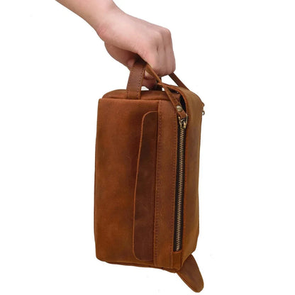Leather toiletry bag held by hand, showing front zip and side strap detail