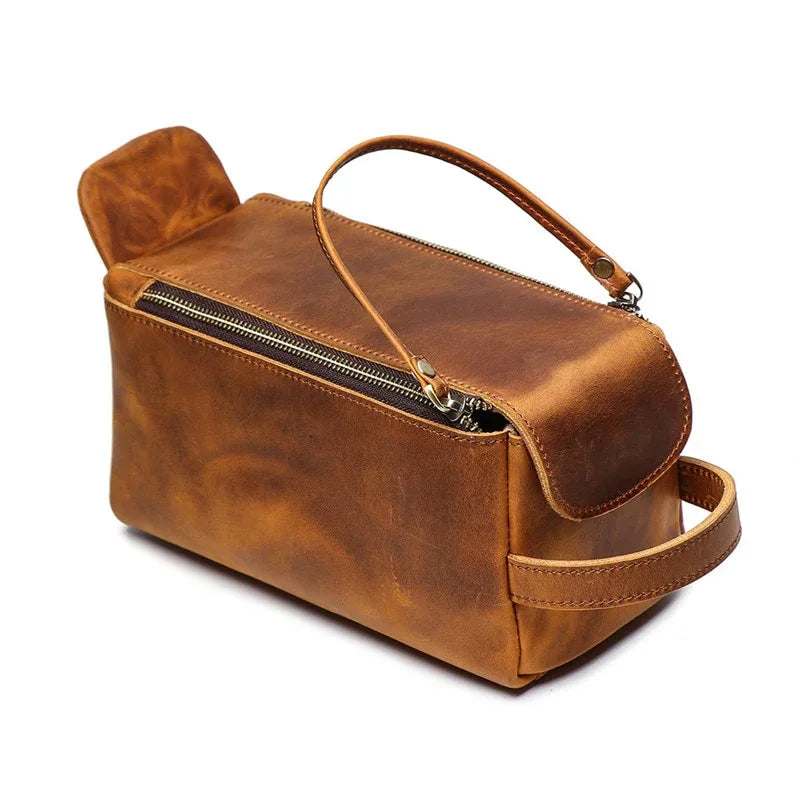 Tan leather toiletry bag with top handle, front double zip, and side strap