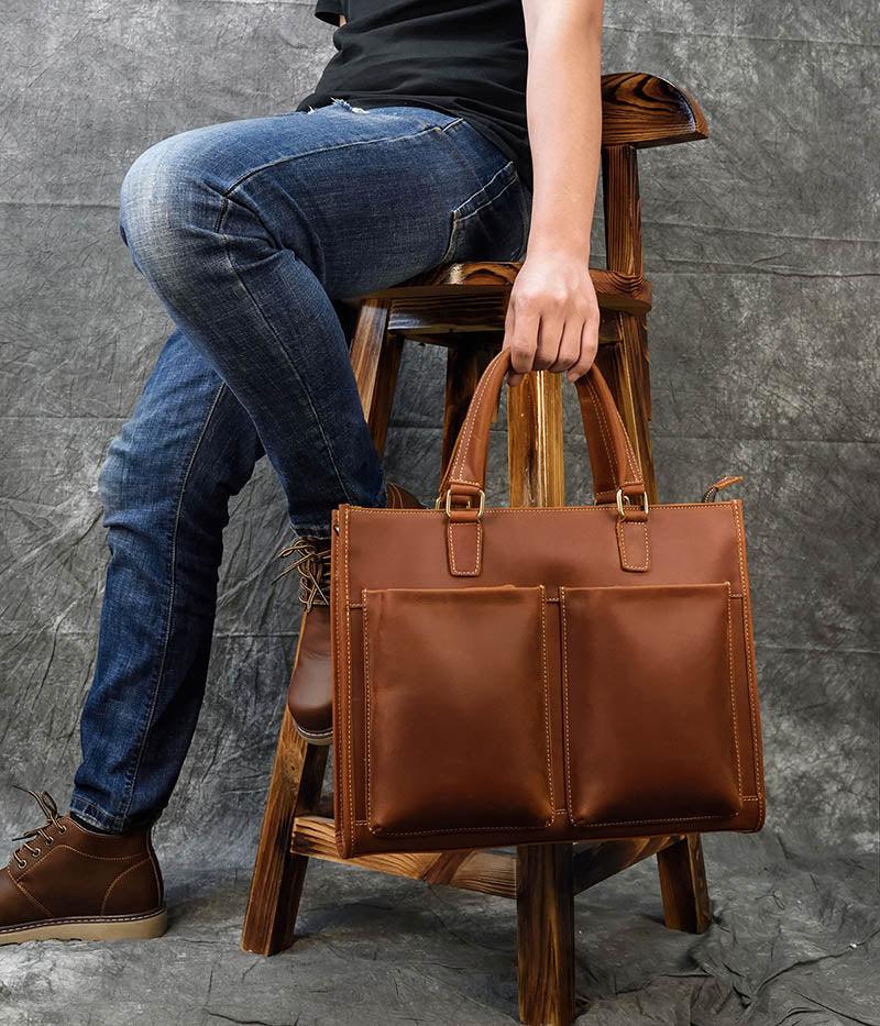 Brown leather messenger bag with shoulder strap and double front pockets, carried in hand