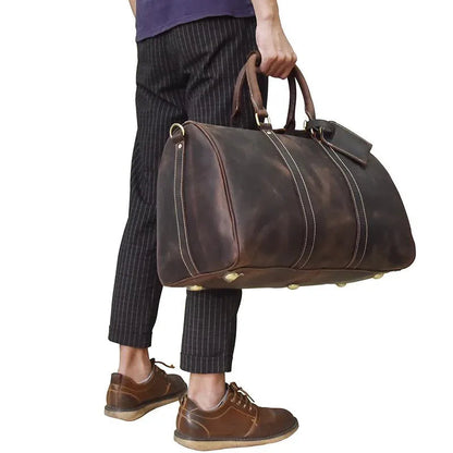 Brown leather duffel bag with dual handles and shoulder strap, held in hand