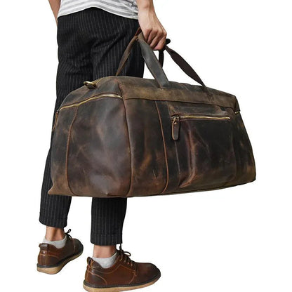 Duffle bag carried by model: brown leather weekender with shoulder strap and front zips.