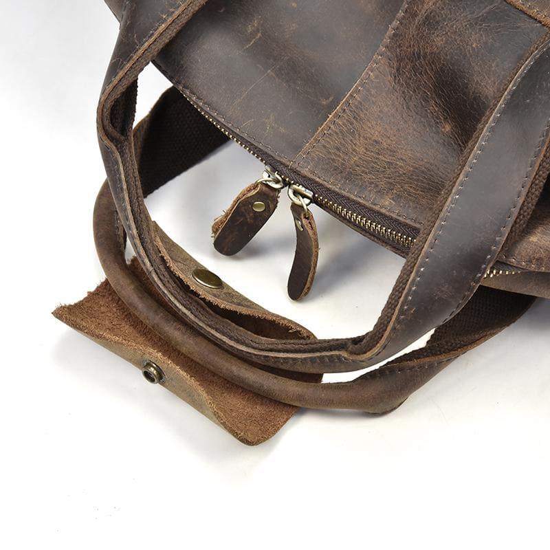 Leather duffle bag corner detail with strap attachments and metal buckles.