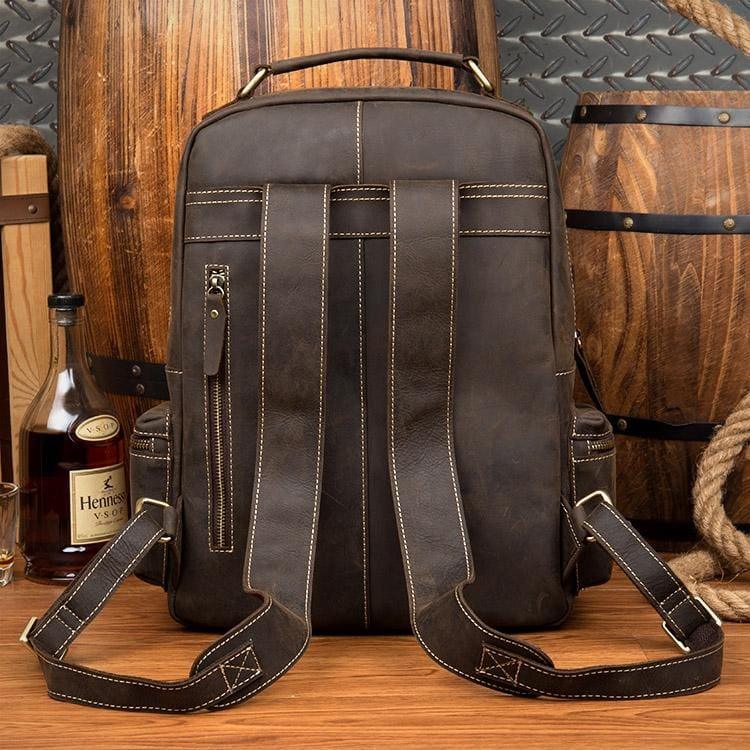 Dark brown leather backpack with stitched front pockets and adjustable crossbody straps.