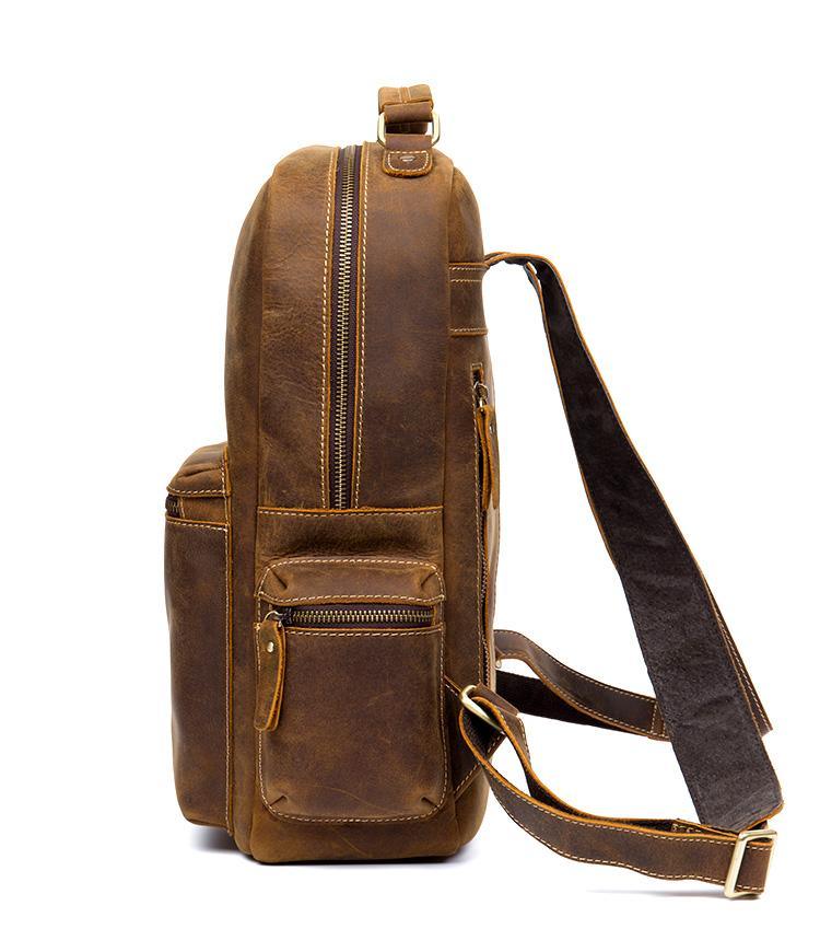 Brown leather backpack with top handle, front zip pocket, and long crossbody strap.