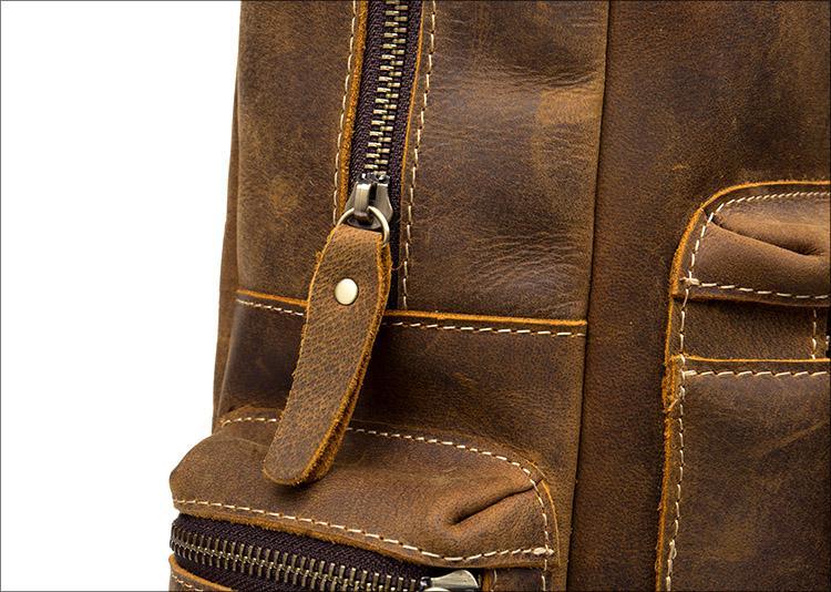 Brown leather backpack detail with front zipper pull tab and stitched pocket panel.