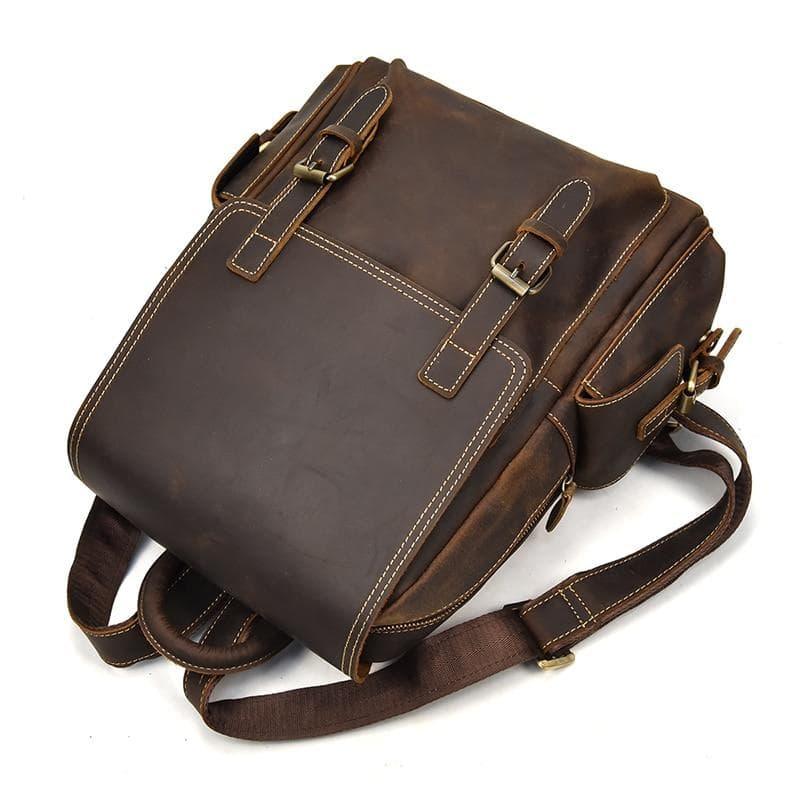Brown leather backpack with top handle, two front buckle straps, and side pocket