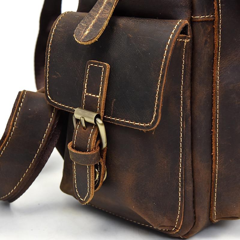 Brown leather backpack close-up of front strap with buckle and stitched flap