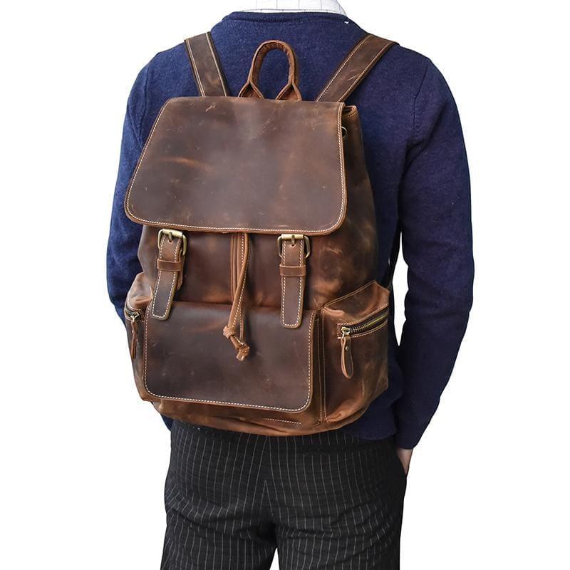 Brown leather backpack worn on back with front flap, buckles, and side zip pocket
