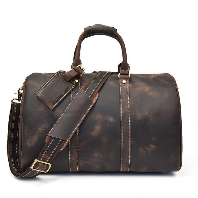 Small dark leather duffle bag with top handle, shoulder strap, and front zip panel