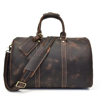 Small dark leather duffle bag with top handle, shoulder strap, and front zip panel