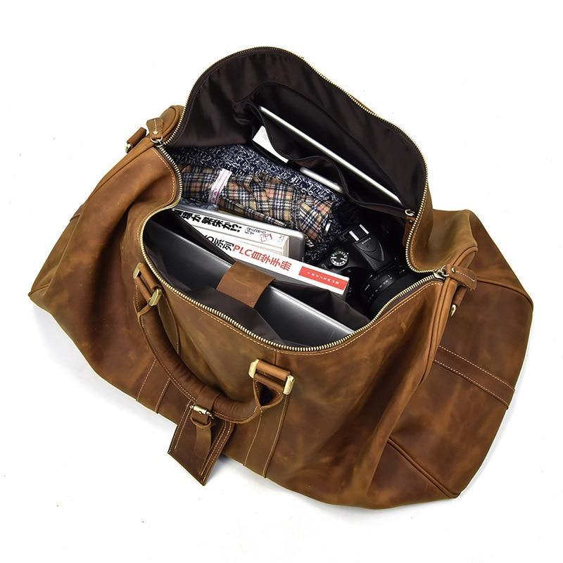 Brown leather duffle bag open to show interior divider, pockets, and zipper compartment.