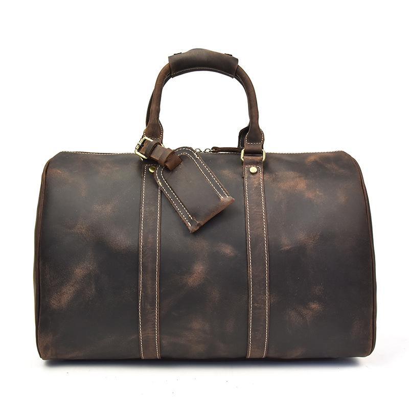 Small dark leather duffle bag with top handles, crossbody strap, and front zip panel
