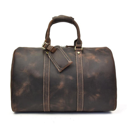 Small dark leather duffle bag with top handles, crossbody strap, and front zip panel