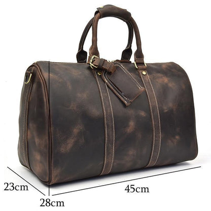 Small dark leather duffle bag with top handles, crossbody strap, and zip side pocket