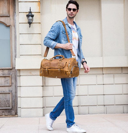 Handmade leather duffle bag in tan brown carried over shoulder with crossbody strap