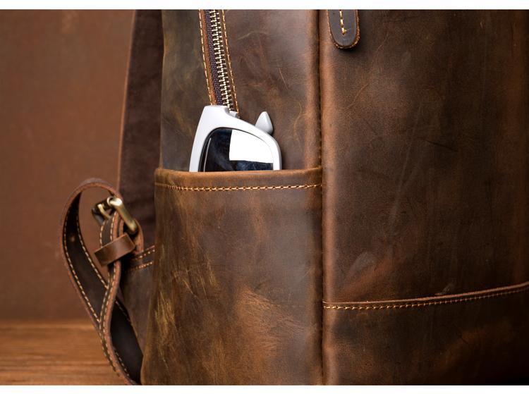 Vintage leather backpack with front pocket holding a white item; zipper and stitching visible