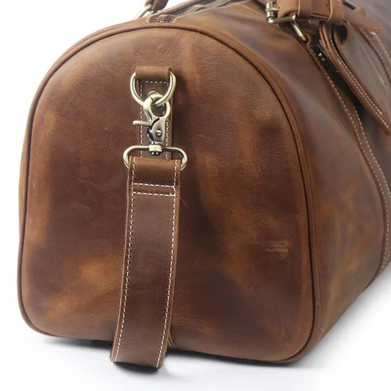 Brown leather duffle bag with front zipper and detachable wrist strap with metal key ring.