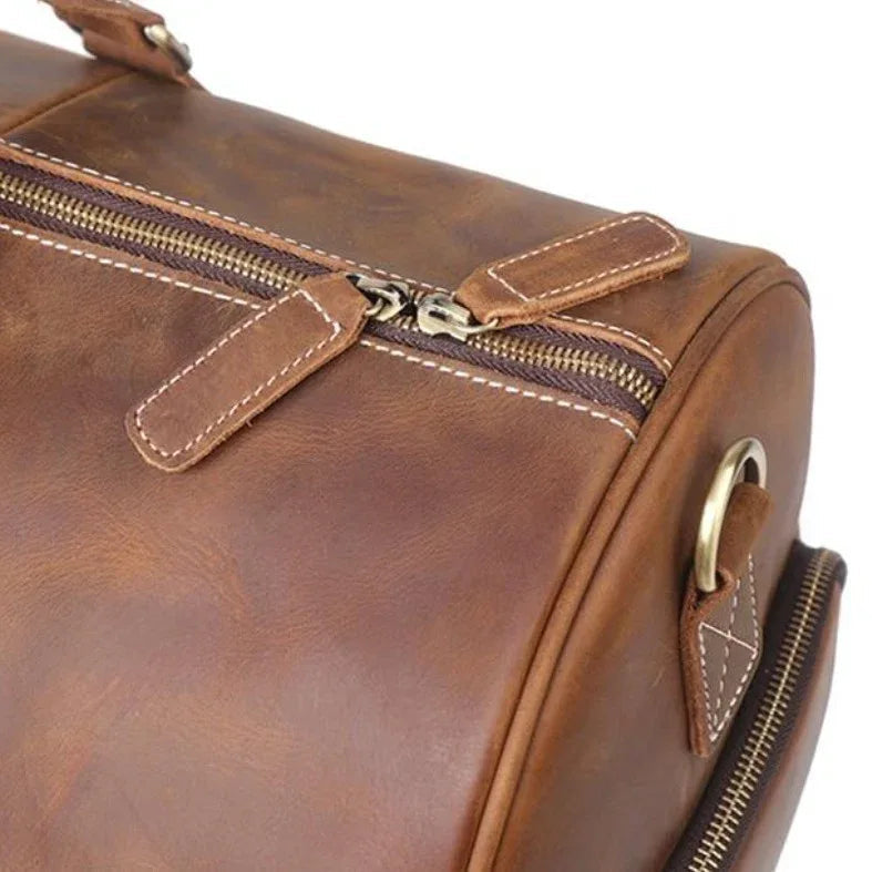 Brown leather duffle bag close-up of double zipper and stitched trim across the top.
