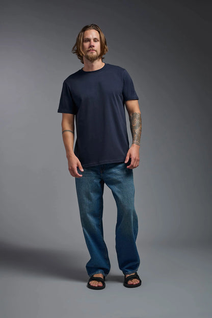 Man wearing a navy t-shirt and blue jeans against a gray background