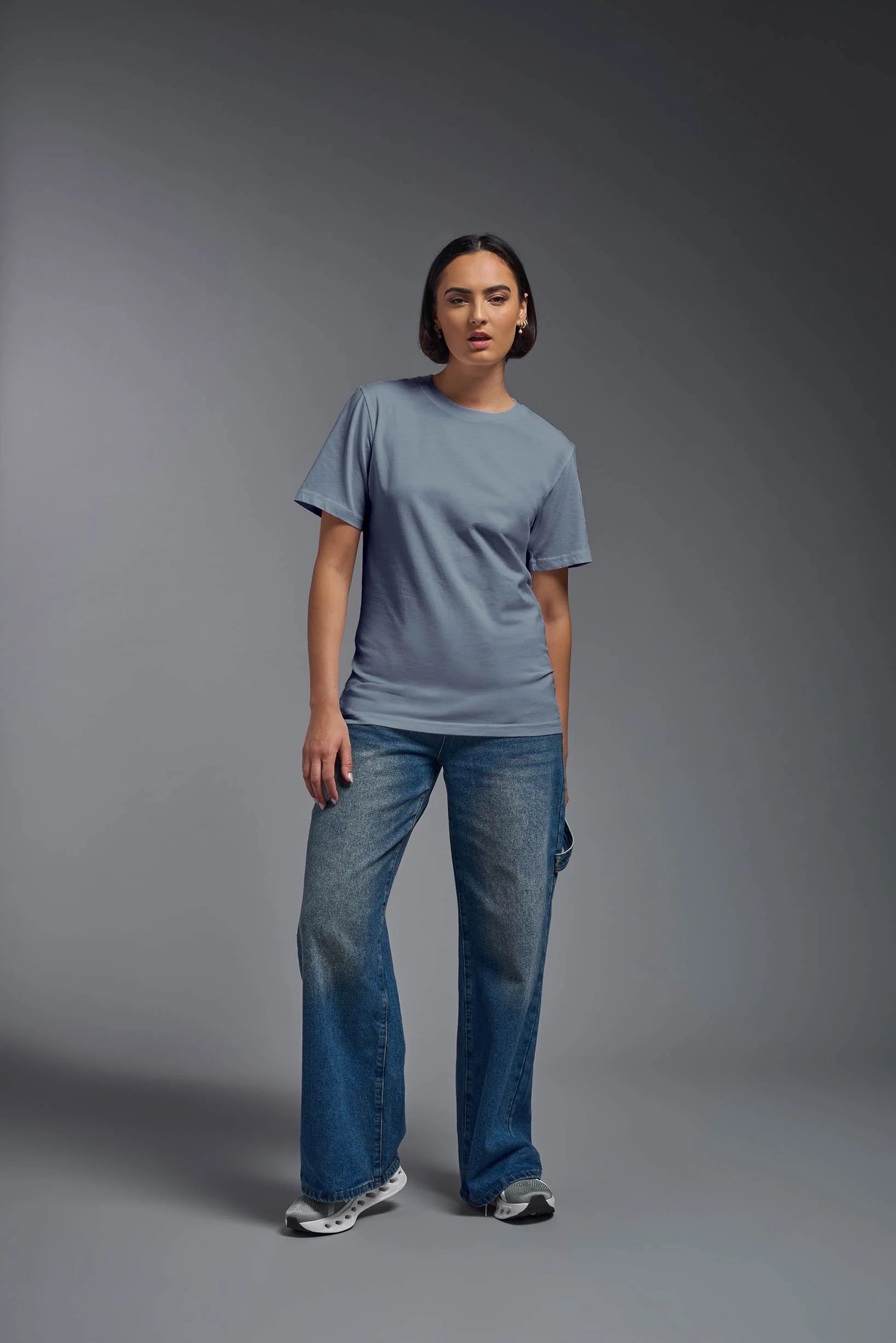 Person wearing a gray t-shirt and blue jeans standing against a gray background