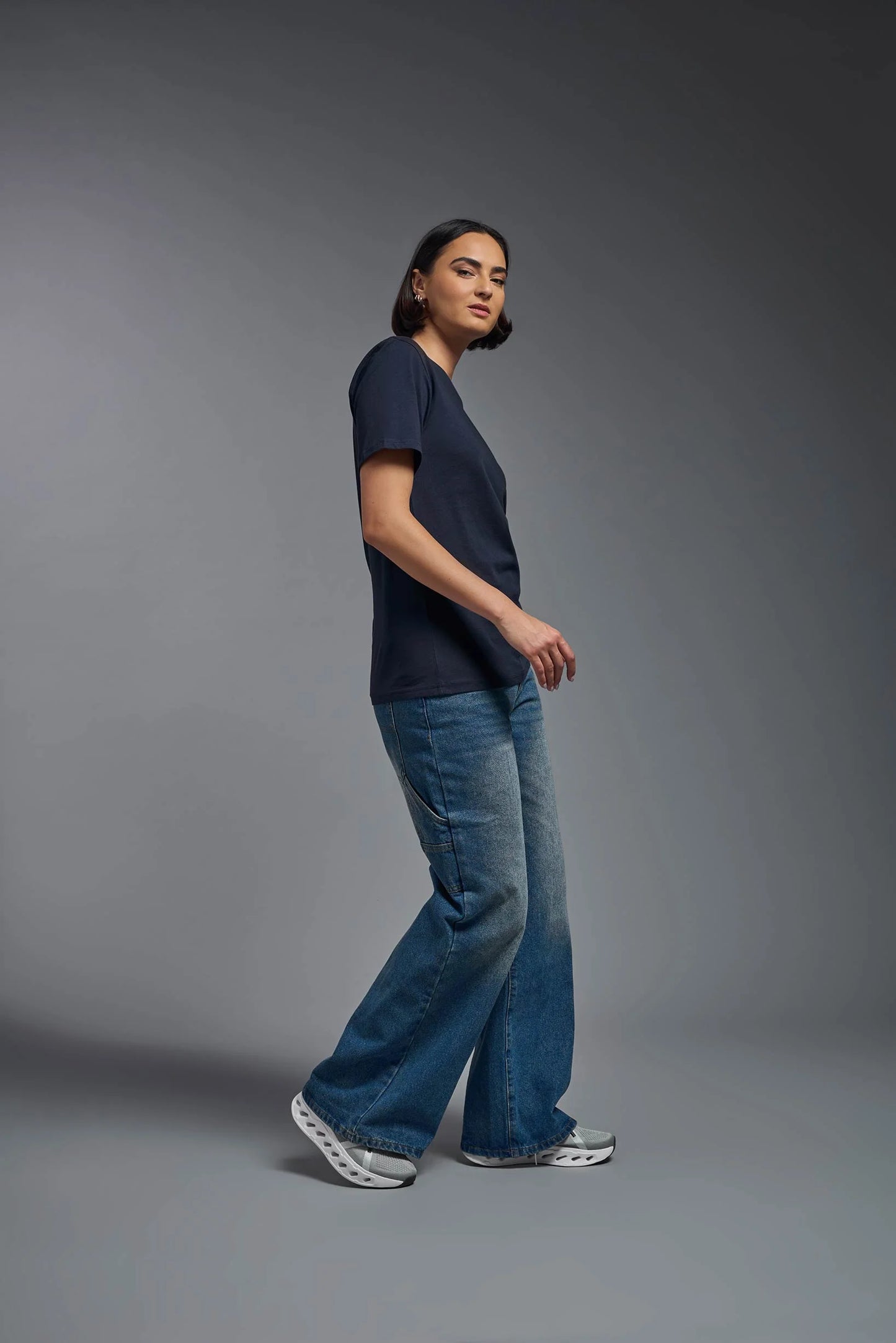 Person wearing a navy t-shirt and blue jeans standing against a gray background