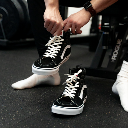 Person tying black and white sneakers on a gym floor.