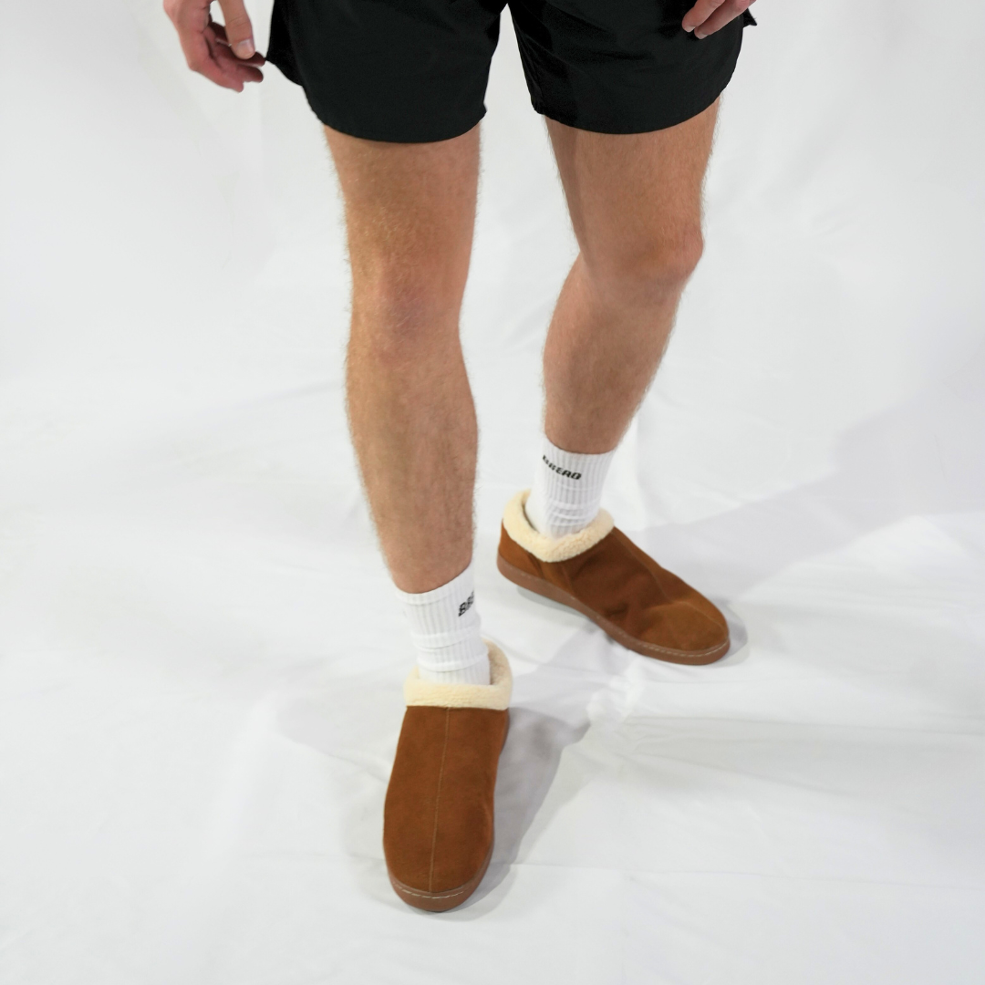 Person wearing brown slippers with white soles on a white background