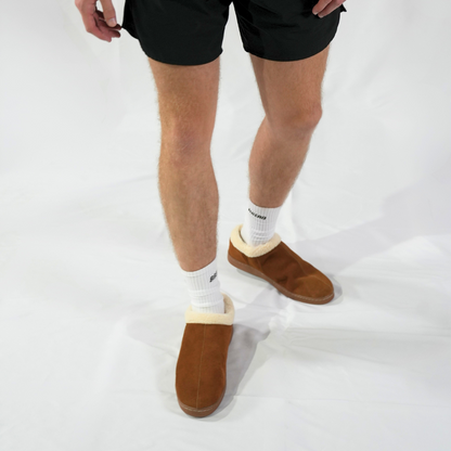 Person wearing brown slippers with white soles on a white background