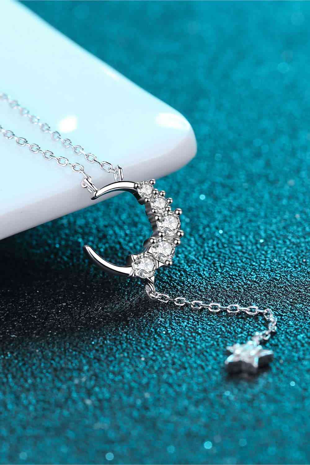 Star & Moon Moissanite Necklace on the side of a table