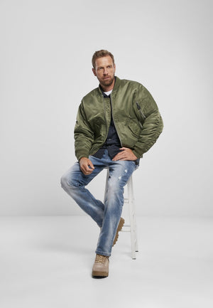 Picture of a Men's MA1 Nylon Bomber Jacket model shot from far away sitting down of the army green color